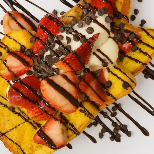 Golden French toast topped with strawberries, whipped cream, chocolate chips, and chocolate drizzle.