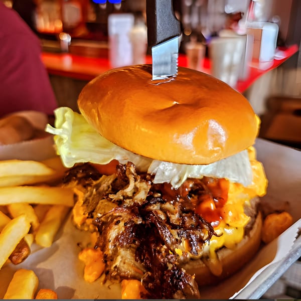 A large diner burger with pulled pork, cheese, lettuce, and a knife, served with fries.
