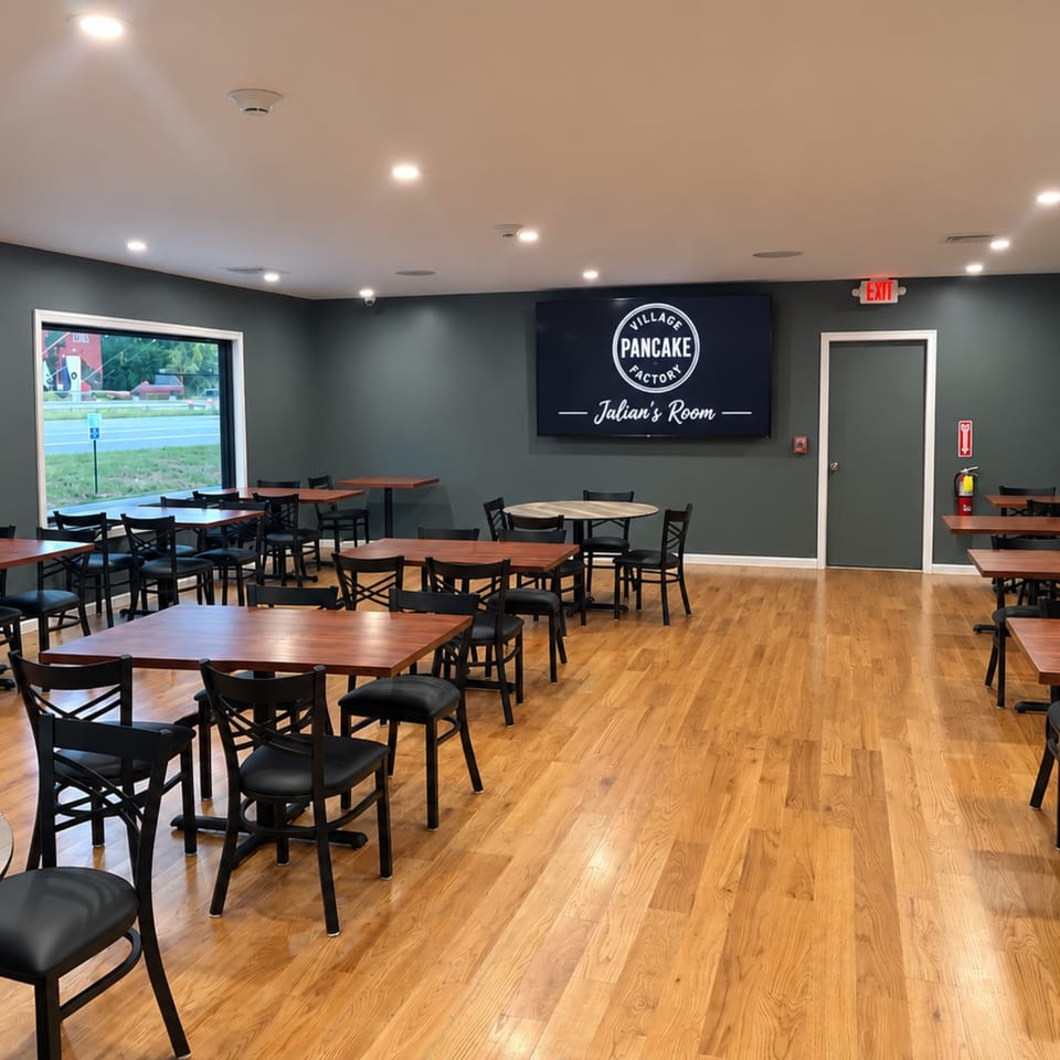 Empty Village Pancake Factory dining room with wooden tables, black chairs, hardwood floors, and Julian’s Room sign.