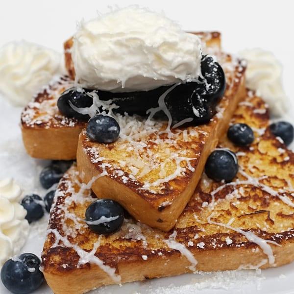 Golden French toast sticks topped with blueberries, whipped cream, and powdered sugar.