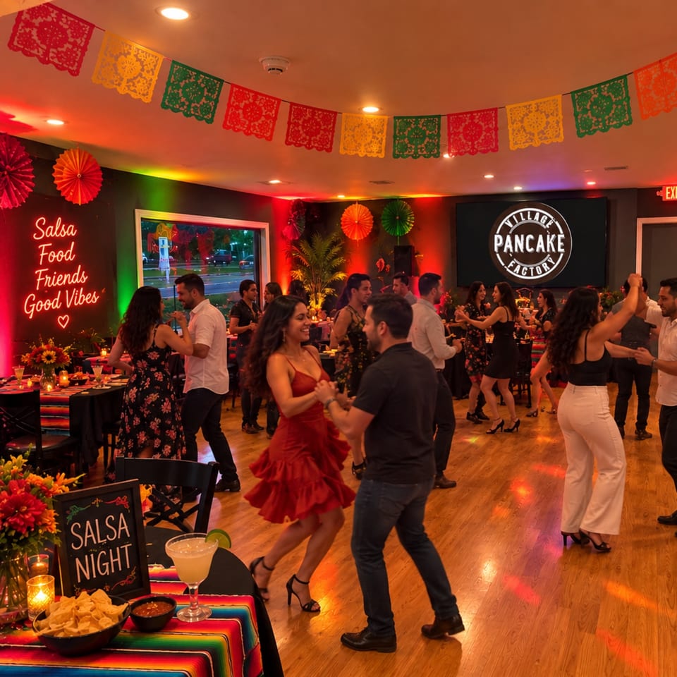 Guests dance during salsa night at Village Pancake Factory, surrounded by colorful Mexican decorations, festive lighting, and a snack table.